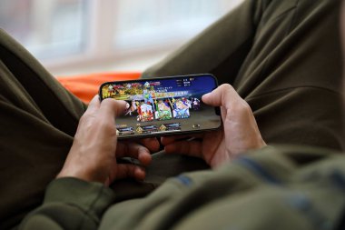 Kader, iPhone 15 akıllı telefon ekranındaki iOS mobil oyun sırasında erkeklerin elinde. Taşınabilir aygıtta mobil oyun ve eğlence