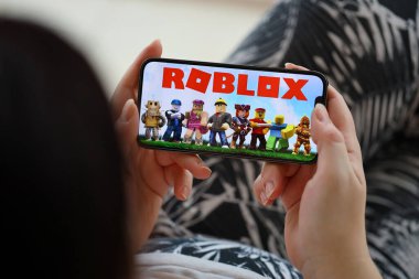 Roblox mobile iOS game on iPhone 15 smartphone screen in female hands during mobile gameplay. Mobile gaming and entertainment on portable device clipart