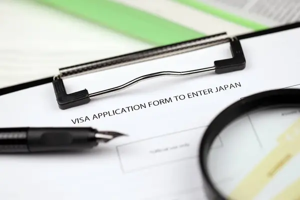 Visa application to enter Japan on A4 tablet lies on office table with pen and magnifying glass close up