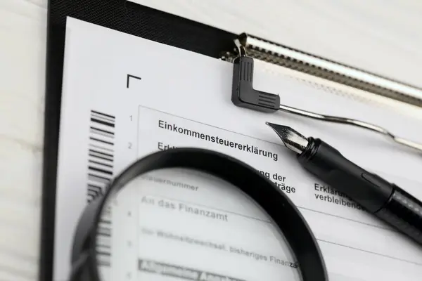 German annual income tax return declaration form blank on A4 tablet lies on office table with pen and magnifying glass close up