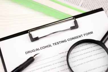 A4 tabletindeki uyuşturucu ve alkol testi onay formu kalem ve büyüteçle birlikte ofis masasının üzerinde duruyor.