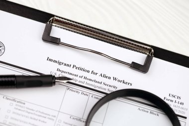 I-140 göçmen dilekçesi A4 tabletindeki yabancı işçiler için boş form kalem ve büyüteçle ofis masasında duruyor.