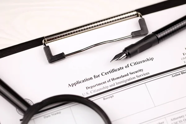 N-600 Application for Certificate of Citizenship blank form on A4 tablet lies on office table with pen and magnifying glass close up