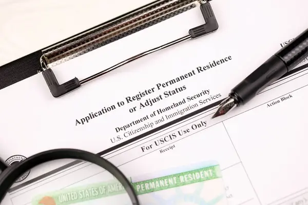 I-485 Application to register permanent residence or adjust status form and green card from dv-lottery on A4 tablet, lies on office table with pen and magnifying glass close up