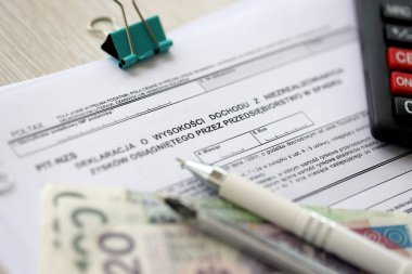 Girişim tarafından miras olarak elde edilen gerçekleşmemiş kar beyannamesi, tükenmez kalem ve cilalı zloti paraları ile muhasebeci masasının üzerindeki PIT-NZS formu