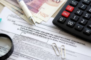 Vergi yılının bireysel aylarında ödenmiş ve vergi kartıyla ödenmiş sağlık sigortası katkı payı beyanı, kalem ve zloti para faturalarıyla dolu muhasebeci masasının PIT-16A formu