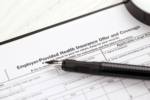 IRS Form 1095-C Employer-Provided Health Insurance Offer, and Coverage tax blank on A4 tablet lies on office table with pen and magnifying glass close up