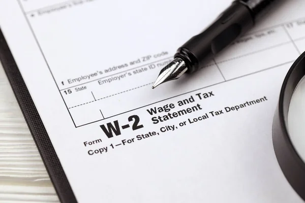 IRS Form W-2 Wage and Tax Statement blank on A4 tablet lies on office table with pen and magnifying glass close up