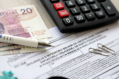 Vergi yılının bireysel aylarında ödenmiş ve vergi kartıyla ödenmiş sağlık sigortası katkı payı beyanı, kalem ve zloti para faturalarıyla dolu muhasebeci masasının PIT-16A formu