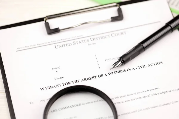 District court warrant for the arrest of a witness in a civil action papers on A4 tablet lies on office table with pen and magnifying glass close up