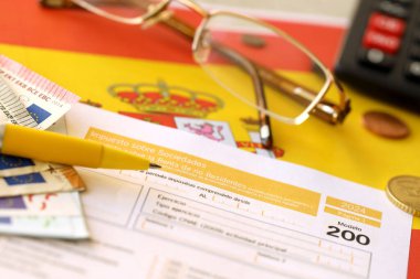 Modelo, vergi mükelleflerinin kurumsal gelir vergisi için 200 İspanyol vergi formu İspanya bayrağında muhasebeci masasına yakın duruyor.