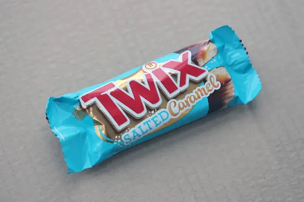 TERNOPİL, UKRAINE - 7 Temmuz 2023 Twix, ahşap zemin üzerinde tuzlu ve mavi karamel ambalajı. Twix, Mars Inc. 'in karamelli ve sütlü çikolatalı bisküvilerden oluşan bir çikolatadır.