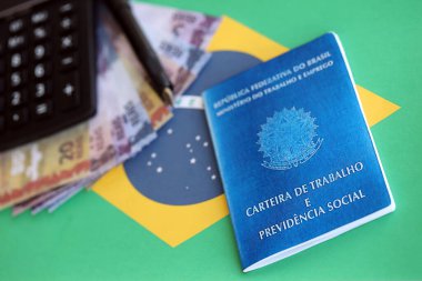 Brazilian work card and social security blue book and reais money bills with calculator and pen on flag of Federative Republic of Brazil close up clipart