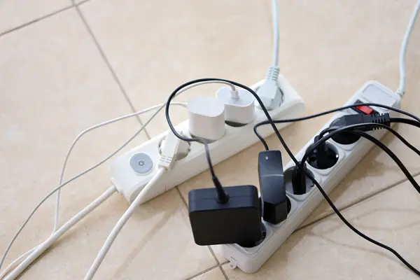 Overloaded power boards. Power strips with different electrical plugs on white floor. Concept of risk danger overloaded current electrical