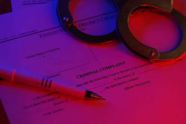 District Court Criminal complaint court papers with handcuffs and blue pen on table close up