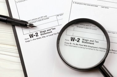 IRS Formu W-2 Maaş ve Vergi beyanı A4 tabletinin üzerinde boş duruyor. Kalem ve büyüteçle kapatılıyor.