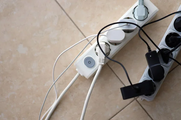 Overloaded power boards. Power strips with different electrical plugs on white floor. Concept of risk danger overloaded current electrical