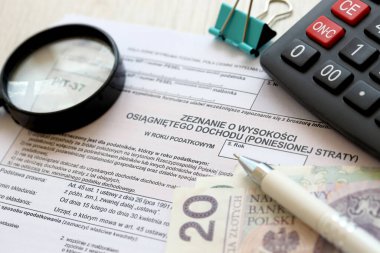 Kazanılan gelir ya da zarar miktarının beyanı, muhasebeci masasının üzerindeki PIT-37 vergi formları ve kalem ve zloti para faturalarının kapatılması