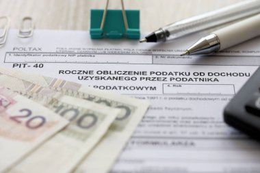 Vergi mükelleflerinin elde ettiği gelir vergisinin yıllık hesaplanması, muhasebeci masasındaki PIT-40 vergi formları ve kalem ve zloti para faturaları kapanıyor