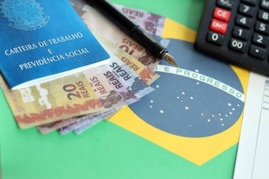 Brezilya iş kartı ve sosyal güvenlik mavi kitap ve hesap makinesi ve Brezilya Federatif Cumhuriyeti bayrağı üzerinde kalem ile para faturaları yakın yakın