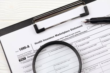 IRS Formu 1095-A Sağlık Sigortası Beyannamesi A4 tabletindeki vergi beyannamesi ofis masasında kalem ve büyüteçle birlikte duruyor.