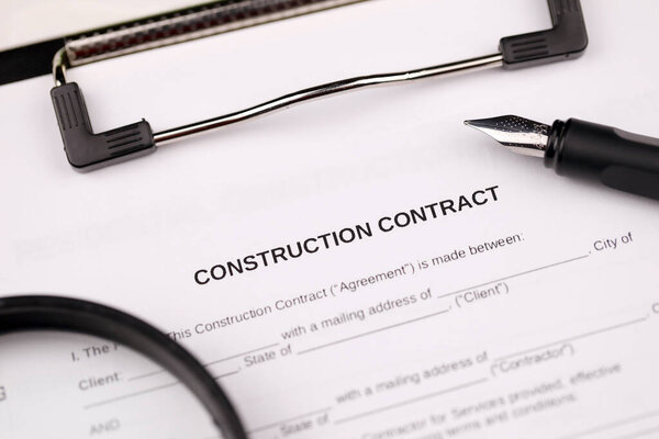 Construction contract form on A4 tablet lies on office table with pen and magnifying glass close up