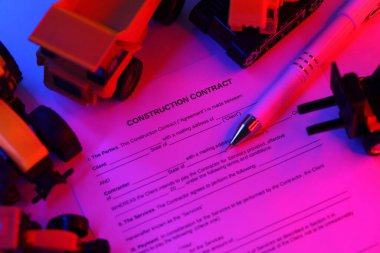 Kalemle yapılan inşaat sözleşmesi birçok sarı inşaat ve servis oyuncağı aracıyla masada duruyor.