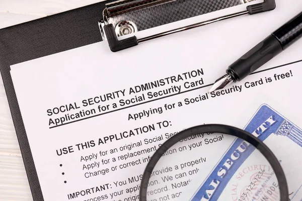 United States social security number cards lies on Application from social security administration on A4 tablet lies on office table with pen and magnifying glass close up