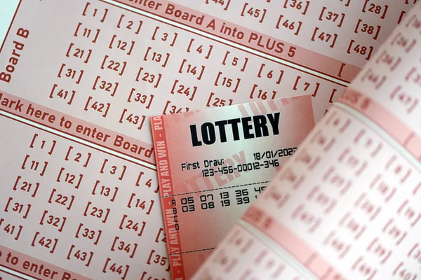 Red lottery ticket lies on pink gambling sheets with numbers for marking to play lottery. Lottery playing concept or gambling addiction. Close up photo