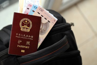 Çin Halk Cumhuriyeti 'nin kırmızı pasaportu ve sırt çantasında uçak biletleri olan Çin Yuan' ı. PRC pasaportu