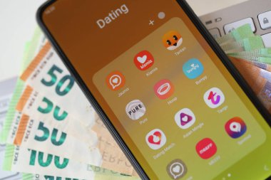 KYIV, UKRAINE - FEBRUARY 28, 2024 Dating apps icons on smartphone display on MacBook keyboard and euro bills clipart