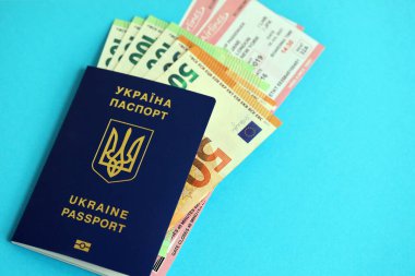 Ukrayna biyometrik pasaportu ve Avrupa Avro para faturaları ve mavi arka planda uçak biletleri.