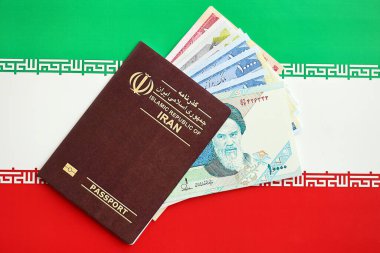 Red Islamic Republic of Iran passport and iranian reals money bills background close up. Tourism and travel concept clipart