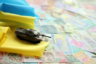 Ukrayna bayrağında farklı para birimlerinde oyuncak tankı. Ukrayna 'daki savaş finansmanı ve askeri destek fiyatlarının geçmişi