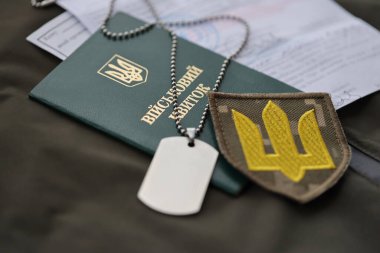 Military token or army ID ticket with mobilization notice lies on green ukrainian military uniform indoors close up clipart