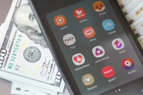 Stock image KYIV, UKRAINE - FEBRUARY 28, 2024 Dating apps icons on smartphone display on MacBook keyboard and US dollar bills