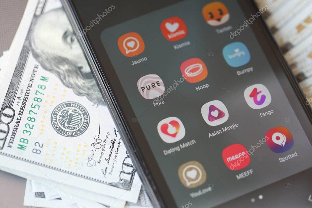 KYIV, UKRAINE - FEBRUARY 28, 2024 Dating apps icons on smartphone display on MacBook keyboard and US dollar bills