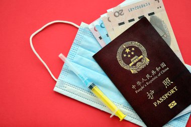 Çin Halk Cumhuriyeti 'nin kırmızı pasaportu ve şırıngalı ve maskeli Çin Yuan paraları. Parlak arkaplanda PRC Çin pasaportu
