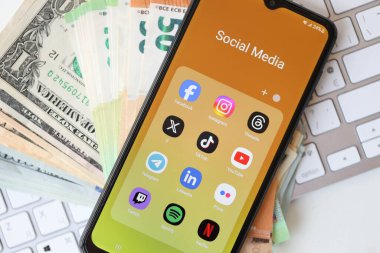 KYIV, UKRAINE - Galaksi A04 'te 28 Şubat 2024 Sosyal Medya simgeleri grubu MacBook klavyesi ve ABD Doları ve Euro banknotları üzerinde akıllı telefon görüntüsü