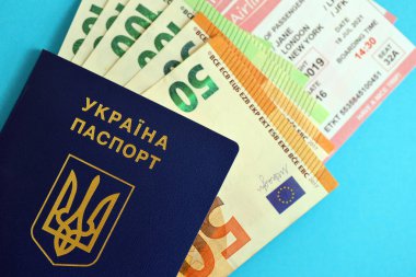 Ukrayna biyometrik pasaportu ve Avrupa Avro para faturaları ve mavi arka planda uçak biletleri.