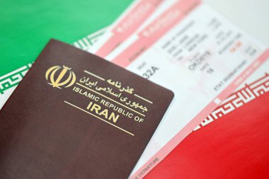 İran Kızıl İslam Cumhuriyeti pasaportu ve İran bayrağı arka planında uçak biletleri. Turizm ve seyahat kavramı