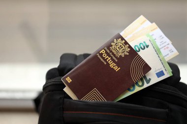 Avrupa Birliği 'nin kırmızı Portekiz pasaportu. Turistik sırt çantasında para ve uçak biletleri var. Turizm ve seyahat kavramı