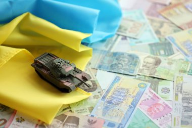 Ukrayna bayrağında farklı para birimlerinde oyuncak tankı. Ukrayna 'daki savaş finansmanı ve askeri destek fiyatlarının geçmişi