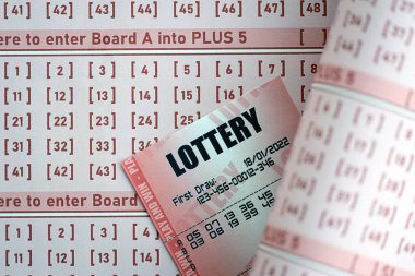 Red lottery ticket lies on pink gambling sheets with numbers for marking to play lottery. Lottery playing concept or gambling addiction. Close up photo