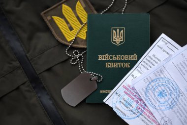 Military token or army ID ticket with mobilization notice lies on green ukrainian military uniform indoors close up clipart