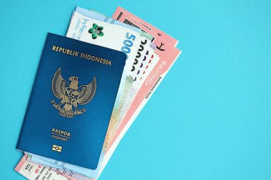 Blue Republic Endonezya pasaportu, mavi arka planda para ve uçak biletleri. Turizm ve seyahat kavramı