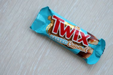TERNOPİL, UKRAINE - 7 Temmuz 2023 Twix, ahşap zemin üzerinde tuzlu ve mavi karamel ambalajı. Twix, Mars Inc. 'in karamelli ve sütlü çikolatalı bisküvilerden oluşan bir çikolatadır.