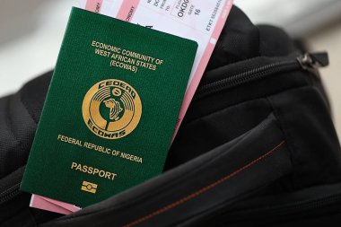 Green Nigerian passport with airline tickets on touristic backpack close up. Tourism and travel concept clipart