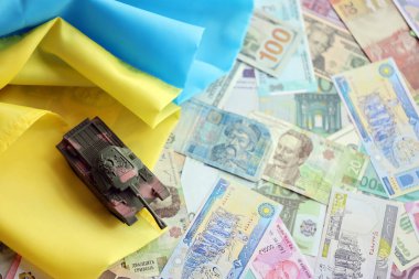 Ukrayna bayrağında farklı para birimlerinde oyuncak tankı. Ukrayna 'daki savaş finansmanı ve askeri destek fiyatlarının geçmişi
