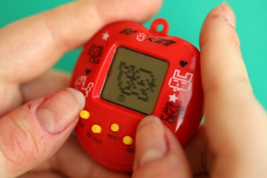 KYIV, UKRAINE - 9 Mart 2024 Retro evcil hayvan zinciri oyunu tamagotchi kırmızı plastik çantada kadınların elinde yakın plan